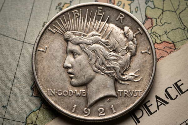 A 1921 High Relief Peace Silver Dollar resting on a vintage world map next to a piece of sheet music titled "PEACE".